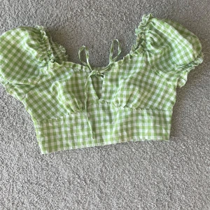 Grön rutig blus - Söt grön rutig blus med puffiga kortärmar och volangdetaljer. Toppen är croppad och har en knytning framtill. Perfekt för sommarens varma dagar.