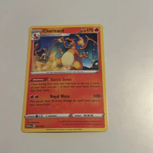Charizard Pokémonkort - Säljer ett Charizard Pokémonkort med 170 HP. Kortet har förmågan 'Battle Sense' och attacken 'Royal Blaze'. Det är ett eld-typ kort med en färgglad illustration av Charizard i en stridsscen. Perfekt för samlare eller spelare som vill förstärka sin kortlek.