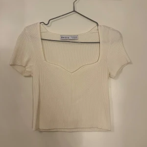 Vit ribbad topp från Bershka - Säljer en stilren vit ribbad topp från Bershka. Toppen har en fyrkantig urringning och korta ärmar, perfekt för en trendig look. Passar bra till både jeans och kjol.