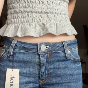 Lågmidjade jeans från Acne - Snygga blå jeans från Acne med klassisk femficksdesign och knappgylf. De har en stilren look med en mörk tvätt och subtila detaljer. Perfekta för en trendig vardagsstil. De är lågmidjade och långa på mig som är 167cm. Fråga om fler bilder och ge gärna prisförslag! Oanvända så lappen är kvar!