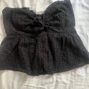 Svart axelbandslös topp - Snygg svart axelbandslös topp med broderade detaljer och knyt framtill. Perfekt för sommarens varma dagar. Toppen har en elastisk rygg för bättre passform. Det står storlek s på lappen men jag anser den mer som en xs men passar för fler storlekar då den har en elastisk rygg🫶 