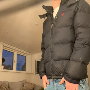 Mörkblå dunjacka från Polo Ralph Lauren - Säljer en snygg mörkblå dunjacka från Polo Ralph Lauren. Den har en broderad röd logga på bröstet och dragkedja framtill. Jackan är i storlek XS men passar även mycket bra för Storlek S. ☺️. Hör gärna av er för mer frågor!!!!