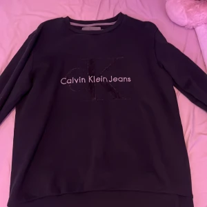 Svart tröja från Calvin Klein Jeans - Säljer en stilren svart tröja från Calvin Klein Jeans med deras ikoniska logga på framsidan. Tröjan har långa ärmar och en rund halsringning. Perfekt för en avslappnad look.