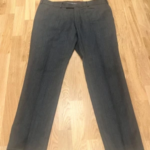 Grå kostymbyxor från Oscar Jacobson - Snygga grå kostymbyxor från Oscar Jacobson i mycket bra skick. Perfekta för både formella tillfällen och kontoret. De har en klassisk passform med dragkedja och knappar. Materialet känns lyxigt och hållbart. Midjemått: 94 cm
