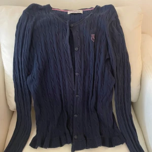 Mörkblå kofta från Hampton Republic - Säljer en snygg mörkblå kofta från Hampton Republic. Den är ribbad med knappar framtill och har en liten logga på bröstet. Perfekt för höst och vår, och den är i mycket bra skick. Passar både till vardags och lite finare tillfällen.