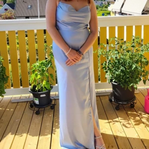 Ljusblå maxiklänning - Elegant ljusblå långklänning med en slits framtill. Perfekt för speciella tillfällen så som bal, fest eller liknade. Har använt den 1 gång så den är som ny! Som referens så är jag 167cm och har 4cm klackar på mig😃 vanligtvis har jag M i kläder och den här klänningen satt perfekt. Det är tunna axelband som korsas i ryggen med en dold dragkedja. 