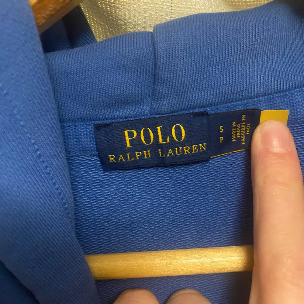 Säljer en snygg blå hoodie från Ralph Lauren med en färgglad broderad logga på bröstet. Tröjan har en klassisk känguruficka och justerbar huva med vita snören. Perfekt för en avslappnad stil.. Tröjor & Koftor.