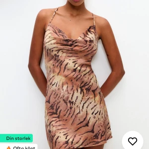 Tigermönstrad klänning med snörning - Trendig kort klänning med tigermönster och smala axelband. Klänningen har en öppen rygg med snygg snörning och är perfekt för en djärv look.