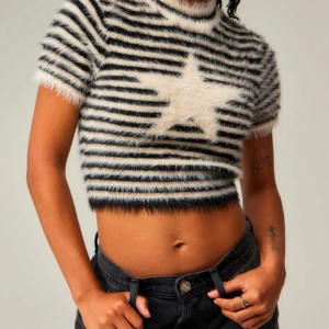 Randig fluffig tröja med stjärna - Säljer en supermjuk och fluffig randig tröja med en stor vit stjärna på framsidan. Tröjan är kortärmad och croppad, perfekt för en trendig look. Den har en cool svart och vit färgkombination som verkligen sticker ut.