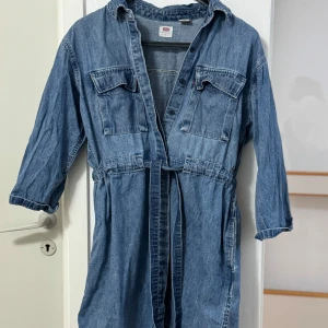 Jeansklänning från Levi's - Snygg jeansklänning från Levi's med knappar framtill och knytskärp i midjan. Klänningen har trekvartsärmar och två bröstfickor. Perfekt för en avslappnad stil.