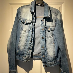 Blå jeansjacka från ONLY - Snygg blå jeansjacka från ONLY med klassisk design och knappar framtill. Jackan har två bröstfickor med lock och knapp samt en bekväm passform.