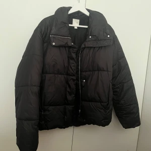 Svart pufferjacka - Snygg svart pufferjacka med dragkedja och knappar. Perfekt för kyliga dagar med sin quiltade design och långa ärmar. Jackan har en hög krage för extra värme och stil. Storlek XS men oversized och passar mig som brukar vara S 
