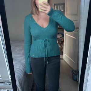 Grön stickad tröja med knyt - Snygg grön stickad mohair tröja med v-ringning och knyt i midjan. Perfekt för kyligare dagar med sin långa ärmar och mjuka material.