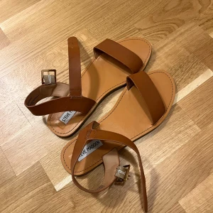 Bruna sandaler från Steve Madden - Snygga bruna sandaler från Steve Madden med justerbart spänne. Perfekta för varma sommardagar. Tillverkade i syntetmaterial för en stilren look.