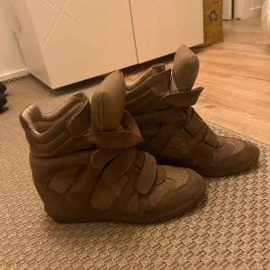 Isabel Marant Bekett skor  - Är lite grönare i verkligheten. Säljer ett par snygga bruna sneakers från Isabel Marant i mocka. De har en cool design med vadderade detaljer och kardborreband för en unik look. Perfekta för höst och vår, och de är i bra skick. Passar både till vardags och lite mer uppklädda tillfällen.