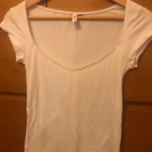 Vit topp från Nelly - Säljer en enkel och stilren vit topp från Nelly. Den har en rundad hals och korta ärmar, perfekt för vardagsbruk eller sommarens varma dagar. Toppen är i ett mjukt och bekvämt material.