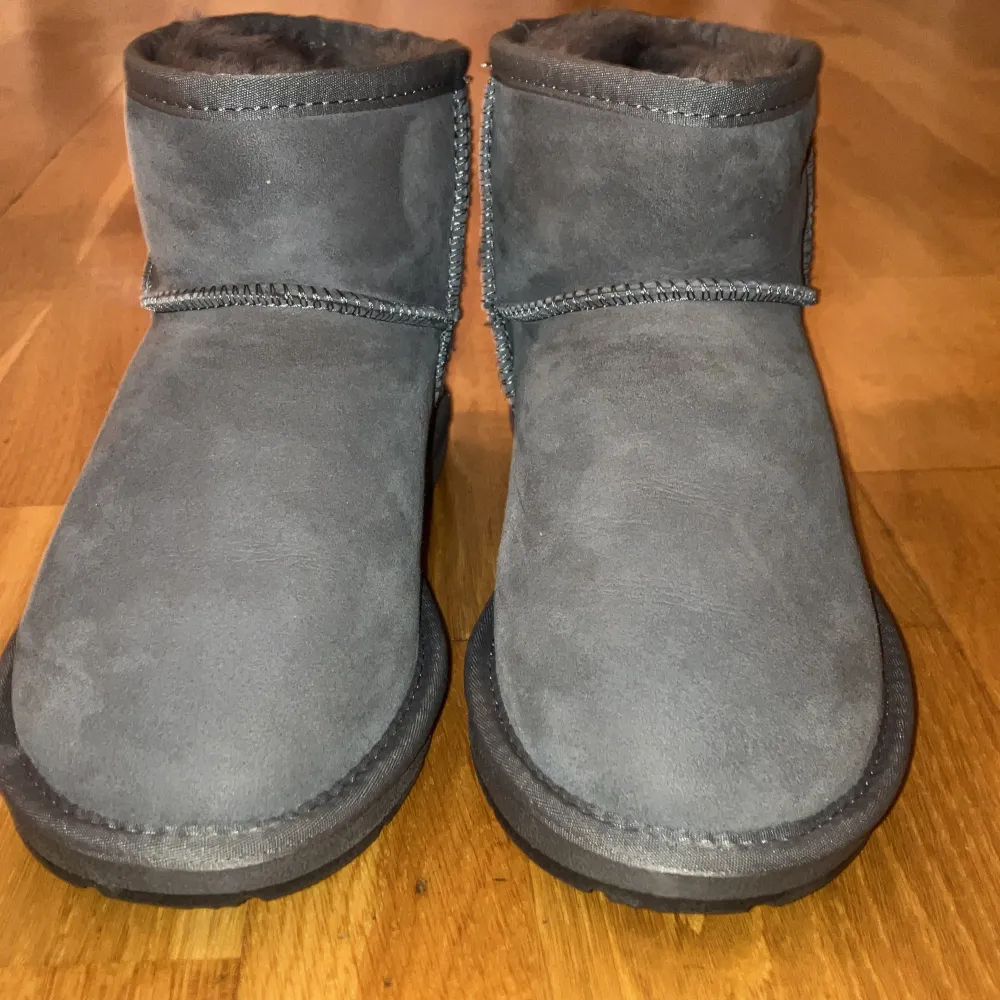 Säljer ett par grå UGG boots i mocka, perfekt för kalla dagar. De är i mycket bra skick och har en mjuk insida som håller fötterna varma. Passar perfekt till höst- och vinteroutfits. Storlek är inte angiven, men de ser ut att vara i normal passform.. Skor.