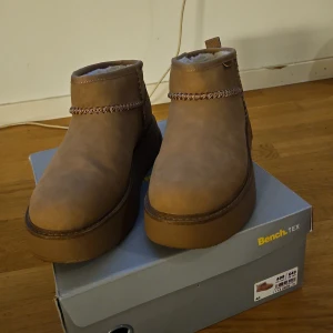 Bruna boots från Bench - Säljer ett par snygga bruna boots från Bench i storlek 41. De är i syntetmaterial med en mysig fleecefodring inuti, perfekt för kalla dagar. Skorna har en robust sula och en stilren design med dekorativ söm runt skaftet. Perfekta för höst och vinter! Skorna har används en gång och har blivit behandlade för vatten. 