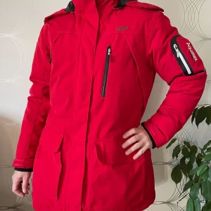 Röd softshelljacka från Aquatex - Säljer en snygg röd softshelljacka från Aquatex i mycket bra skick. Jackan har långa ärmar och en praktisk dragkedja framtill. Perfekt för höst och vinter med sin varma och skyddande design. Den har också en cool ficka med dragkedja på ärmen.