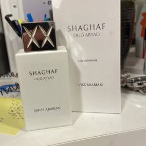 Shaghaf Oud Abyad Eau de Parfum - Shaghaf Oud Abyad från Swiss Arabian är en elegant Eau de Parfum med en lyxig och intensiv doft. Flaskan är vit med en stilren design och ett silverfärgat lock med X-mönster. Perfekt för den som söker en unik och kraftfull doftupplevelse.