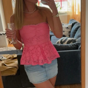 Rosa spets tubtopp - Säljer en söt rosa tubtopp i spets med volangdetaljer. Perfekt för sommarens fester och tillfällen. Toppen är axelbandslös och har inlägg.