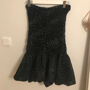 glittrig klänning från Maje - Intressekoll på min älskade Maje klänning, vet ej om jag vill sälja!!! Snygg svart klänning från Maje med glittriga detaljer. Den är axelbandslös och har en volangdetalj vid fållen. Perfekt för nyår! Storlek 36 