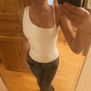 Vit topp - Säljer en stilren vit linnetopp i ett mjukt och stretchigt material. Toppen har en smal ärm och en tight passform, perfekt för sommardagar eller som ett basplagg i garderoben. Passar till både jeans och kjol!