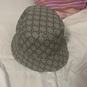 Gucci hatt med monogrammönster - Snygg Gucci hatt med det klassiska monogrammönstret i beige och brunt. Perfekt för att ge din outfit en lyxig touch. Hatten är i mycket bra skick och passar de flesta tack vare sin one size-storlek. Ett måste för alla modeälskare! Den är äkta och vi kan diskutera på priset har knappt använt den en helt ny kostar 5800 och jag säljer den för 3000kr