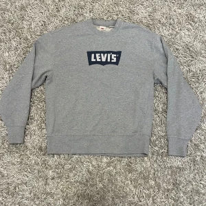 Levi's tröja - Säljer en grå sweatshirt från Levi's i storlek M. Den har en avslappnad passform och ett stort Levi's-tryck på bröstet. Perfekt för en casual look och passar bra till både jeans och joggers. Tröjan är i mycket bra skick och redo för nya äventyr!