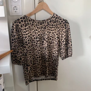 Leopardmönstrad topp med trekvartsärm - Säljer en snygg leopardmönstrad topp med trekvartsärm. Perfekt för att ge din outfit en vild touch! Toppen är i ett mjukt material och har en normal passform. Passar både till vardags och fest. 🐆✨