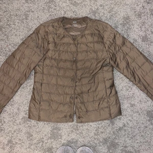 Brun dunjacka från Uniqlo - Säljer en lätt och smidig brun dunjacka från Uniqlo. Perfekt för lager-på-lager under höst och vår. Jackan har långa ärmar och knäppning fram. Den är i bra skick och passar både till vardags och lite finare tillfällen.
