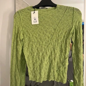 Grön spetsblus från TL Berkey - Snygg grön spetsblus från TL Berkey med långärmad design. Perfekt för att lägga till en touch av elegans i din garderob. Blusen har en unik struktur och är tillverkad i ett vackert spetsmaterial.