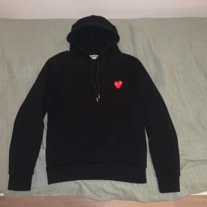 Comme des garçons hoodie - Säljer en snygg svart hoodie från Comme des Garçons Play med rött hjärta på bröstet. Den är i bra skick, knappast använd och perfekt för både höst och vinter. Hoodien har en klassisk passform med långa ärmar och en bekväm huva. Perfekt för en stilren och avslappnad look! Är i storlek S men sitter mer som M och passar bäst personer som är emellan 170-180 cm långa! 