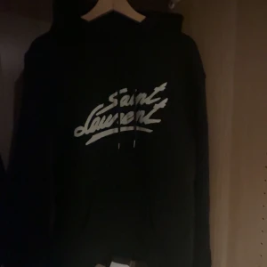 Saint Laurent hoodie - Säljer en snygg svart hoodie från Saint Laurent med deras ikoniska logga på framsidan. Perfekt för en stilren och avslappnad look. Den har en klassisk passform och är superbekväm. Perfekt för både vardag och fest! Saknar tyvärr kvitto då jag köpte på appen. Vill även förtydliga att lapparna va lösa när jag köpte, så jag tog beslutet att klippa av för såg bättre ut på det viset. Helt ny annars. Kan tänkas att förhandla vid snabb affär! 🤝🏽🤩🍾