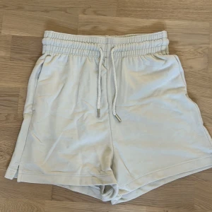 Beige shorts från H&M - Säljer ett par superbekväma beige/vita shorts från H&M i storlek XS. De har en elastisk midja med snörning och små slitsar på sidorna. Perfekta för sommaren eller en avslappnad dag hemma. Materialet är en blandning av bomull och polyester vilket gör dem både mjuka och hållbara.