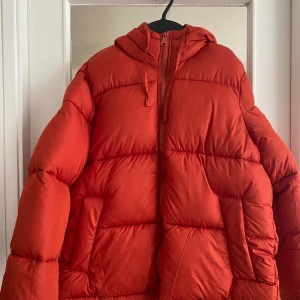 Röd pufferjacka från H&M - Säljer en snygg och varm röd pufferjacka från H&M. Jackan har en dragkedja framtill och en mysig huva. Perfekt för kalla vinterdagar. Jackan är i nyskick och har aldrig använts, prislappen sitter fortfarande kvar. Passar perfekt för dig som vill hålla dig varm och se trendig ut samtidigt!