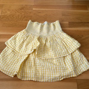 Gul rutig kjol från Kappahl - Säljer en superfin gul rutig kjol från Kappahl. Den har en smockad midja och volanger som ger en söt och somrig look. Perfekt för varma dagar och kan stylas både upp och ner. Kjolen är i bomull och känns väldigt lätt och skön att ha på sig. Passar perfekt till sommaren! 
