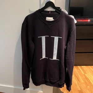 Svart sweatshirt från Les Deux - Säljer en snygg svart sweatshirt från Les Deux med ett stort vitt tryck på framsidan. Tröjan är i bomull och polyester, vilket gör den både bekväm och hållbar. Perfekt för höst och vinter! 🖤