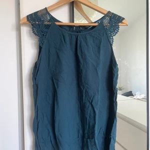 Mörkgrön ärmlös topp med spetsdetaljer - Säljer en snygg mörkgrön/blå topp med fina spetsdetaljer vid axlarna.💕 Toppen är perfekt för både vardag och fest💕Storlek 38, M men passar S med💕 