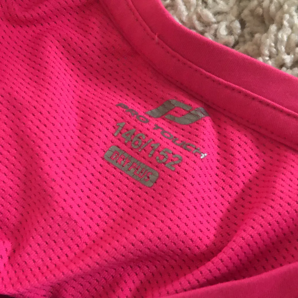 Säljer en rosa tränings t-shirt från Pro Touch i storlek 146-152. T-shirten är gjord av polyester och är perfekt för träning. Den har en normal passform och korta ärmar. Materialet är lätt och andas bra, vilket gör den bekväm att ha på sig under intensiva träningspass. Perfekt för dig som vill ha en färgglad och funktionell tränings t-shirt!. T-shirts.