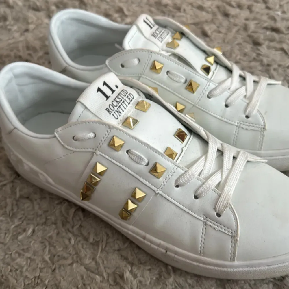 Säljer ett par snygga vita sneakers från Valentino. De har coola guldfärgade nitar som ger en extra edge till looken. Skorna är i bra skick och passar perfekt till både vardag och fest. Storlek 39. Finns inga äktighetsbevis därav priset.🩷. Skor.