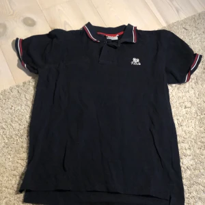 Mörkblå pikétröja från Ebbes - Säljer en snygg mörkblå pikétröja från Ebbes i storlek S. Tröjan har korta ärmar och en klassisk krage med röd och vit randig detalj. Perfekt för både vardag och fest! 🖤
