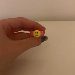 Rosa ring med smiley - Säljer en supergullig rosa ring med en gul smiley på framsidan. Perfekt för att liva upp vilken outfit som helst! Ringen är i plast och passar de flesta storlekar.