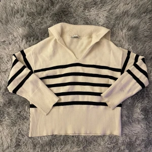 Randig tröja från Zara - Säljer en snygg randig tröja från Zara i krämvitt och svart. Tröjan har en unik krage och långa ärmar med ribbade muddar. Perfekt för en stilren look.