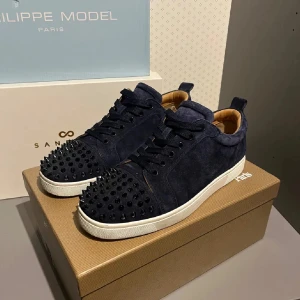 Mörkblå loubs - Snygga mörkblå sneakers från Philippe Model med nitar på tån och en kontrasterande röd sula. Skorna har snörning och är tillverkade i mocka för en lyxig känsla.