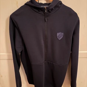 Mörkblå hoodie från Djurgårdens IF - Säljer en mörkblå hoodie (half zip) från Djurgårdens IF med dragkedja och klubbens emblem på bröstet. Perfekt för att visa ditt stöd för laget. Hoodien är mycket skön & som ny (inga skador). Endast använd fåtal gånger då tonåringen vuxit ur den. 