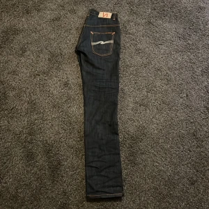 Mörkblå jeans från Nudie Jeans - Säljer dessa Snygga mörkblå jeans från Nudie för jag har vuxit ur dem, dem är inte andvända mycket. Storlek 28M 32L