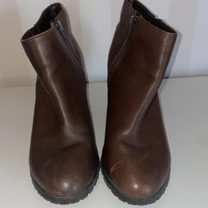 Bruna kilklackade boots med dragkedja - Snygga bruna boots med kilklack och dragkedja på sidan, bra skick st.38. Perfekta för höst och vinter med en robust sula för bra grepp. Tillverkade i skinnliknande material.