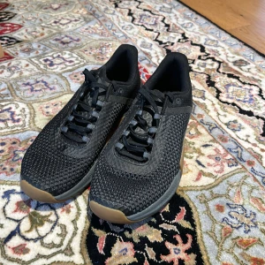 Tyngdlyftningsskor/träningsskor - Snygga svarta sneakers med stickad ovandel och snörning. Skorna har en kontrasterande gummisula i brunt och svart, vilket ger ett stilrent intryck. Perfekta för ett utmärkt träningspass!