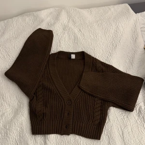Brun stickad kofta från H&M - Säljer en mysig brun stickad kofta från H&M. Koftan har ett flätat mönster längs sidorna och knappar framtill. I storlek XS men passar även S. 